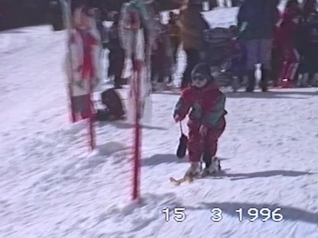 Vintage 1996 footage shows a cute toddler in a red snowsuit falling over while learning to ski before an adult comes to help