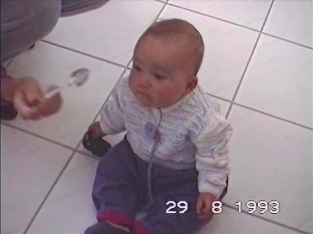 Vintage home video footage shows a mother feeding her baby with a spoon on the floor in 1993