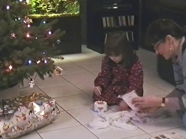 Vintage footage captures a tender moment as a little girl watches her mother unwrap a present by the Christmas tree