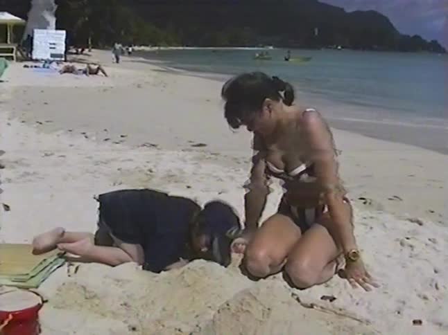 Home video footage captures a mother and child enjoying a day at a tropical beach, playing together in the sand