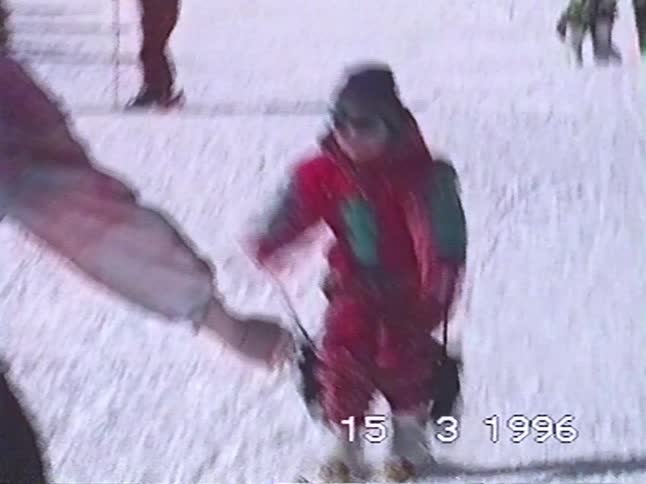 Vintage 1996 home video shows a parent helping their small child learn how to ski on a sunny day at a ski resort