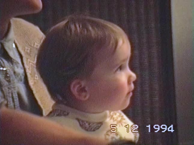 A young baby sits captivated on their mother's lap watching TV in a vintage home video from 1994