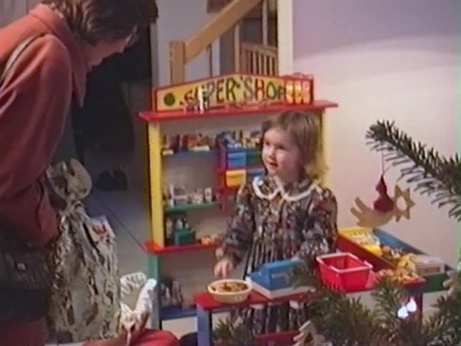 Vintage footage captures a joyful little girl playing shopkeeper with her toy supermarket on Christmas