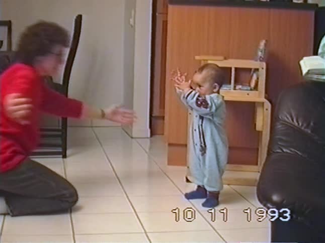 A mother encourages her baby boy to take his first steps in their home in this sweet 1993 home video