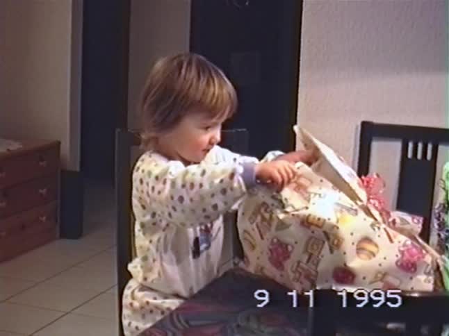 Vintage 1995 home video shows a cute toddler in pajamas excitedly unwrapping a birthday present at a table