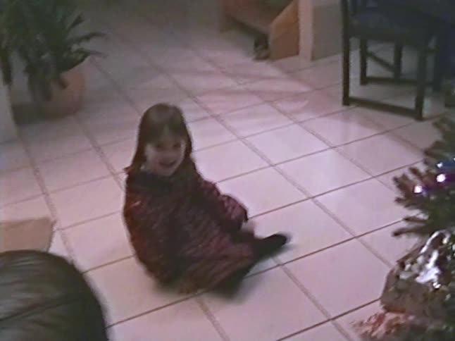 Adorable toddler in a festive dress smiles and crawls toward the camera by the Christmas tree