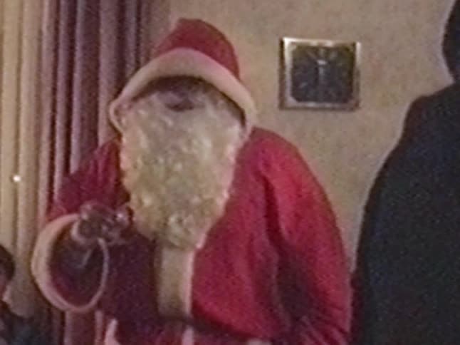 Grainy vintage footage of a man putting on his Santa Claus costume at home
