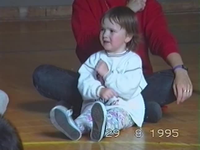 A cute toddler joyfully participates in a music and movement class in 1995, clapping and waving her hands