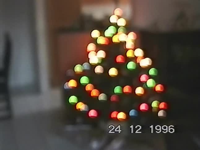 A nostalgic VHS home video from Christmas Eve 1996 shows a slow focus pull revealing a decorated Christmas tree with presents underneath