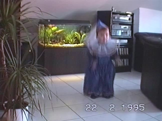 An excited little girl in a sparkly blue costume joyfully dances and waves for the camera in her living room