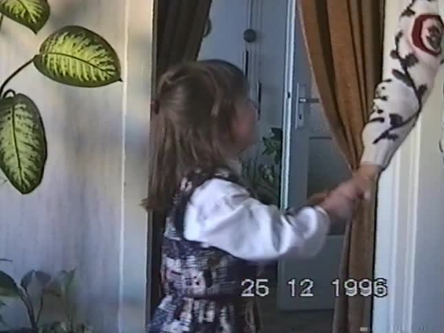 A little girl shyly holds an adult's hand and smiles for the camera in a nostalgic home video from Christmas 1996