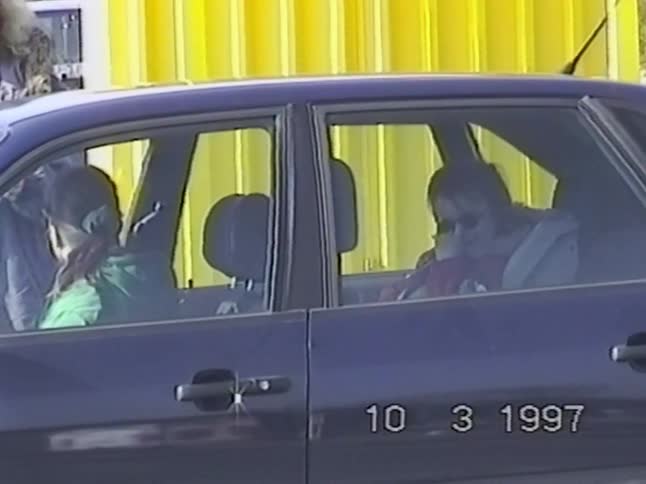 A vintage home movie from 1997 shows two women and a baby sitting in a parked car on a sunny day