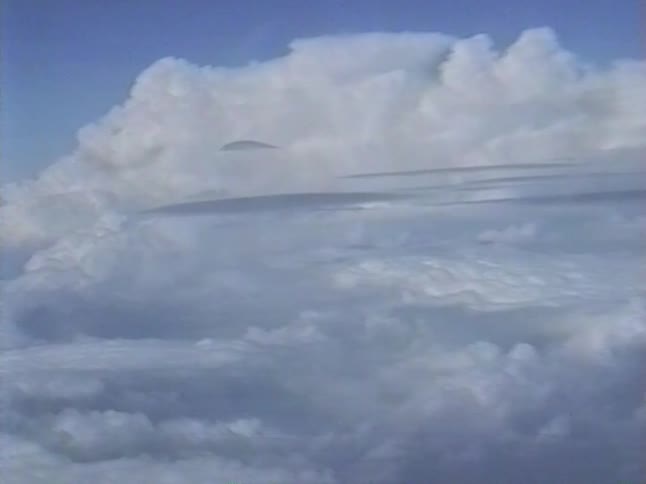 Vintage 1980s aerial footage captures a slow zoom into a massive cloud formation in a clear blue sky
