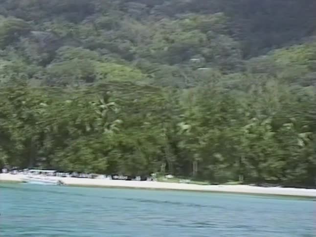 Vintage VHS footage captures a serene tropical island with a white sand beach and lush jungle, as seen from the water