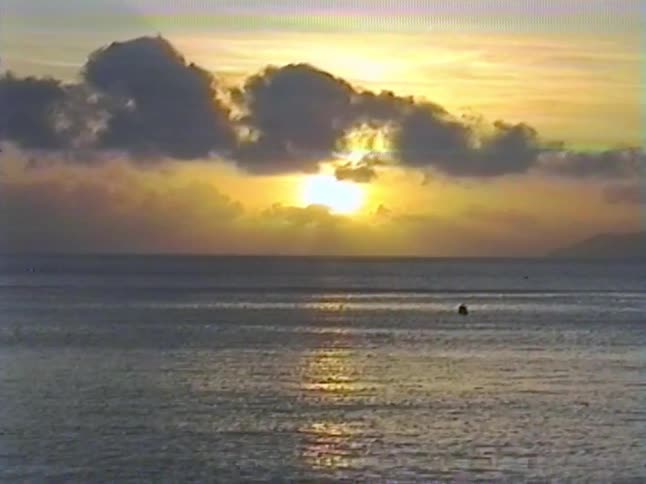 A serene sunset glows over a calm ocean, its golden reflection shimmering on the water in this vintage footage