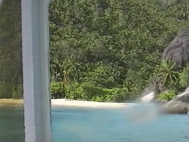 A vintage point-of-view from a boat's window approaching a secluded tropical island with a sandy beach and lush jungle
