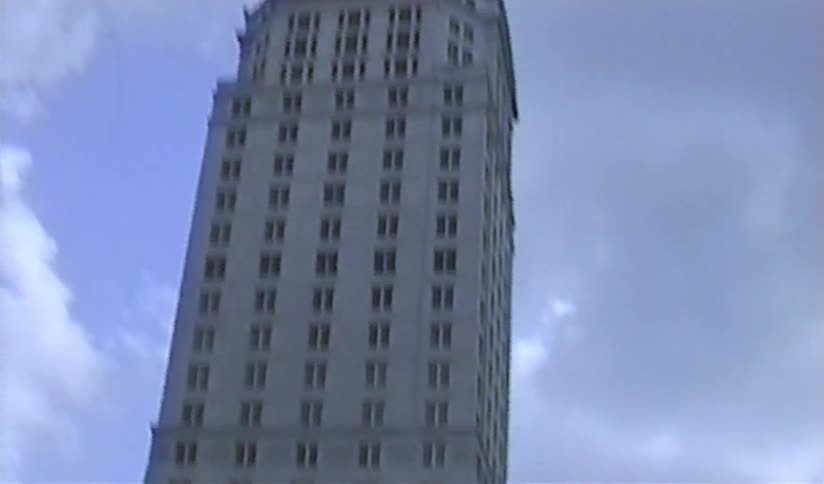 Vintage handheld footage tilts down a historic high-rise building on an overcast day