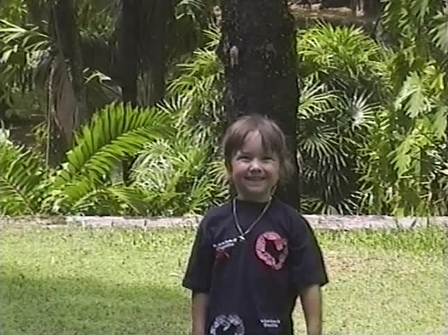 Vintage home video footage shows a cute little girl smiling for the camera in a lush, green park