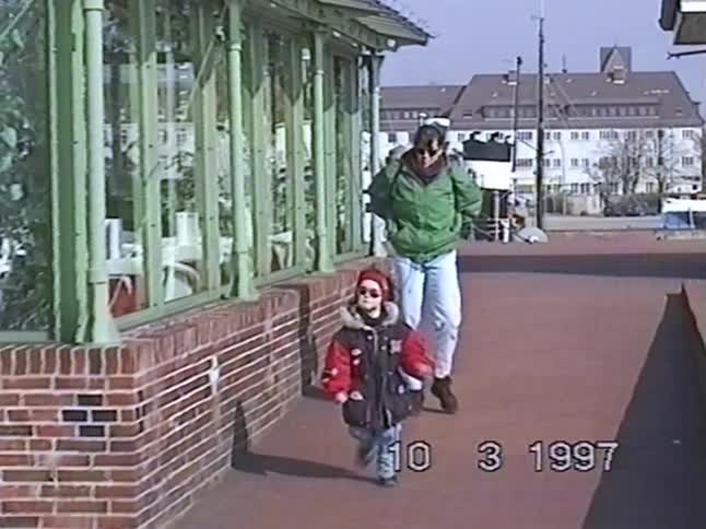 A mother and young child bundled in winter coats walk down a brick path in a city in this vintage 1997 home video
