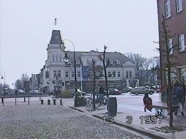 Archival VHS footage from March 1997 shows daily life on a cobblestone street corner in a European town