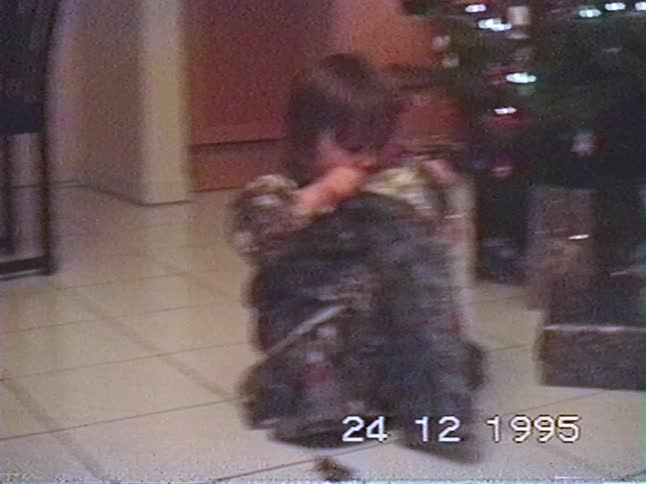 An authentic VHS home video from 1995 shows a little girl excitedly unwrapping a Christmas present by the tree