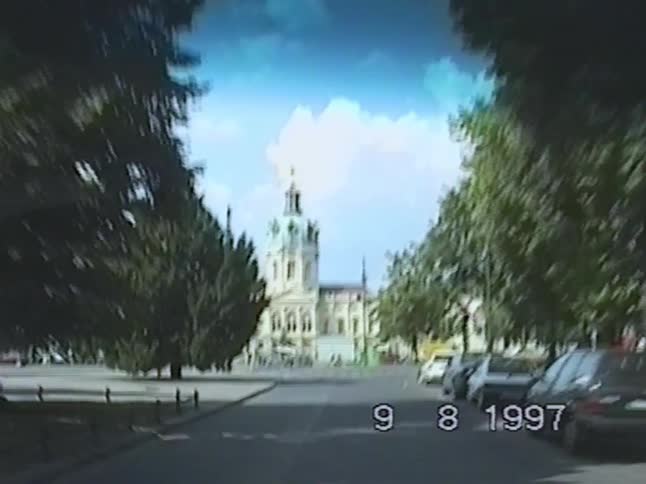 A vintage point-of-view shot from 1997 driving down a beautiful tree-lined street toward the historic Charlottenburg Palace in Berlin, Germany