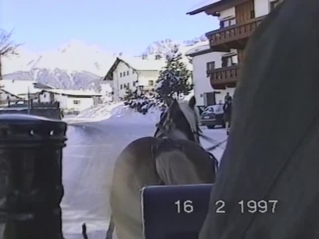 A vintage 1997 clip shows a point-of-view perspective from a horse-drawn sleigh ride through a quaint, snowy mountain village