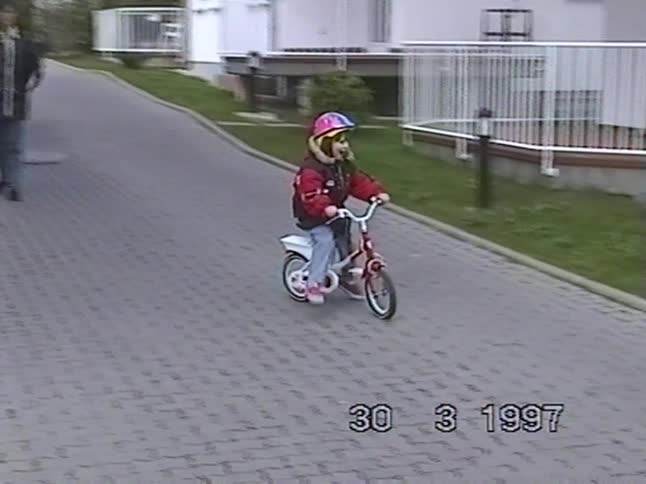 Vintage 1997 home video of a mother teaching her young daughter how to ride her new bicycle in the driveway
