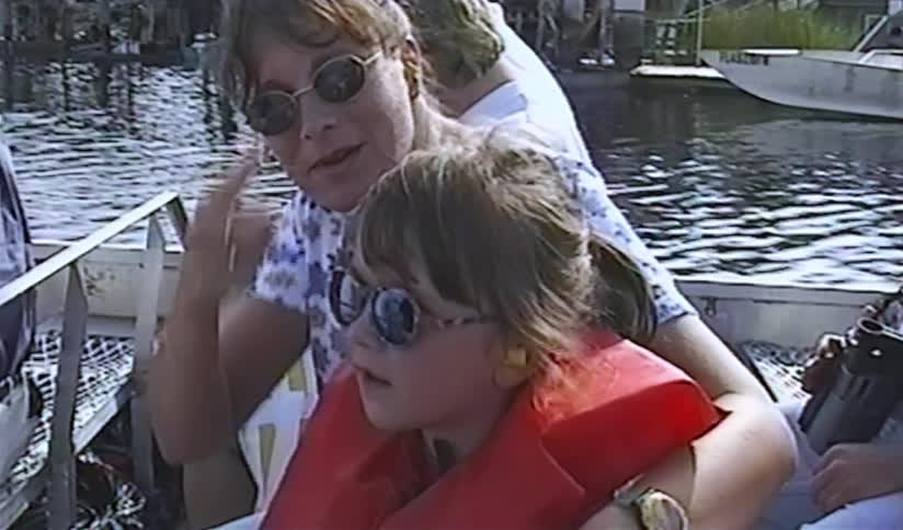 A vintage home movie captures a mother and her young daughter enjoying a sunny day on a fan boat