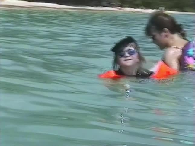 A nostalgic VHS home movie shows a mother and her young daughter playfully swimming together in the turquoise ocean during a tropical vacation