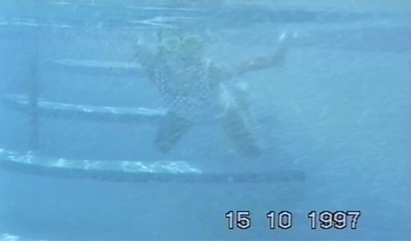 A young girl wearing goggles swims underwater in a swimming pool in this vintage home video from 1997