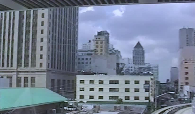 Vintage VHS footage captures a slow pull-back shot of a city skyline with a rooftop parking lot and elevated train tracks on a cloudy day