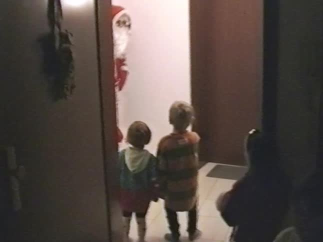Vintage home video captures the magical moment when young children are surprised by Santa Claus appearing in their hallway