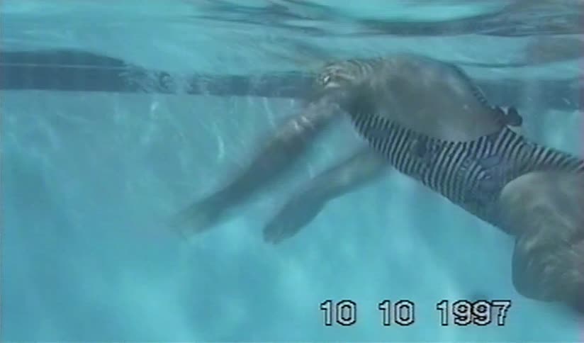 Vintage underwater footage from 1997 shows a person in a striped swimsuit swimming in a pool
