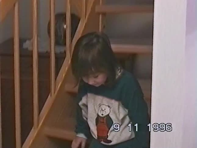 A cute little girl in pajamas smiles for the camera while sitting on a wooden staircase in her home in 1996