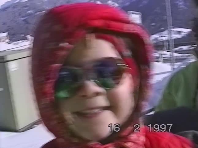 Nostalgic home video from 1997 shows a cute kid in a red hood and reflective sunglasses smiling happily in a snowy landscape