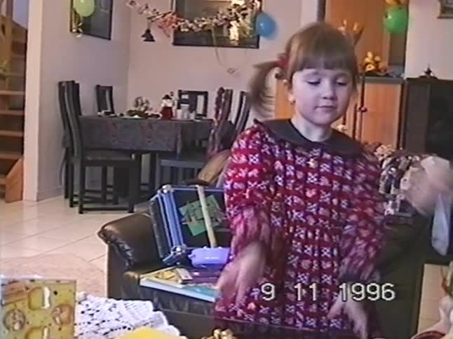 An adorable little girl in a red dress gets her hair put into a ponytail at a birthday party in a 1996 home video