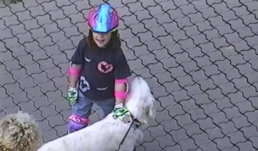 Nostalgic home video footage shows a young girl in colorful rollerblading gear petting her happy white dog