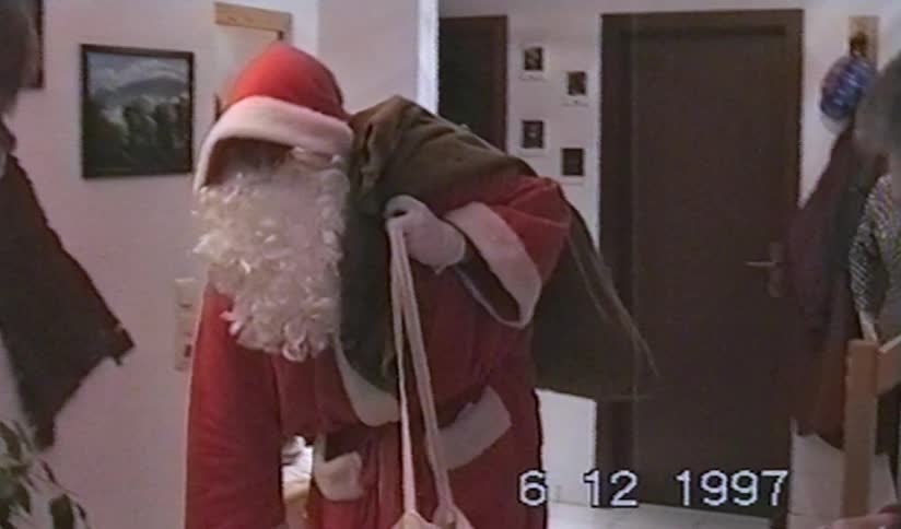 A vintage 1997 home video captures a person dressed as Santa Claus with a large sack of presents in a family's home