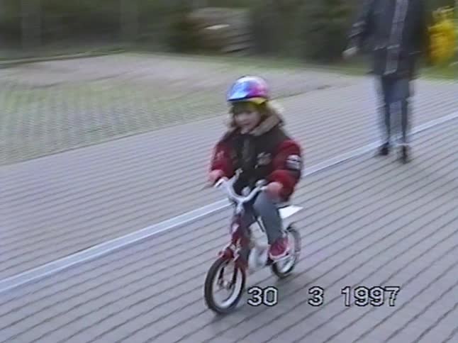 Vintage 1997 home video captures a little girl in a helmet learning to ride her bike with a parent's help