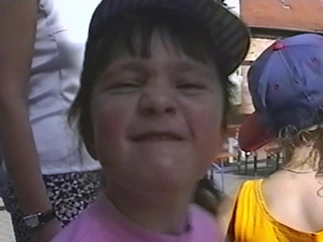 Close-up vintage home video of a cute little girl in a hat making a funny, scrunched-up face for the camera