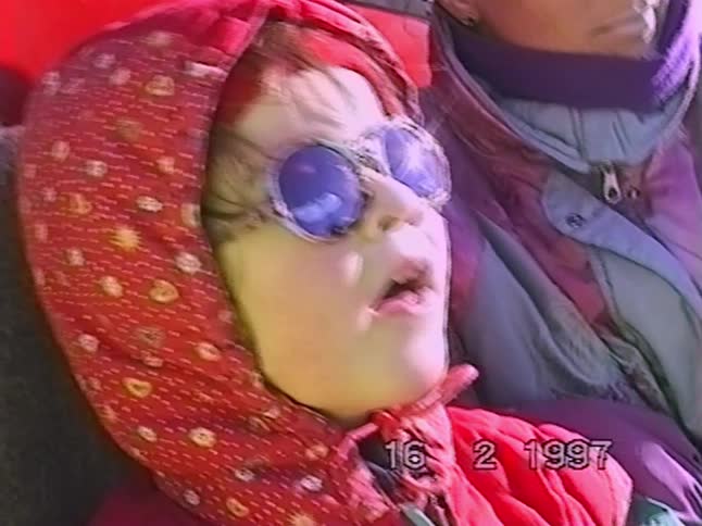 A close-up of a young girl in a red hood and reflective sunglasses on a sunny winter day in 1997