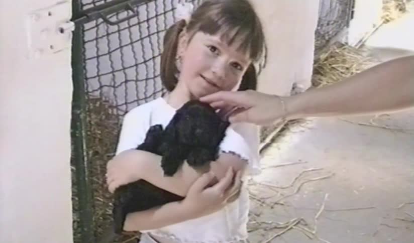 Charming vintage footage shows a sweet little girl with pigtails holding a tiny black puppy in a stable