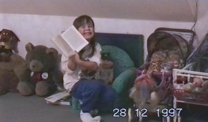 Vintage home video from 1997 shows a cute little girl reading a book in her playroom before breaking into joyful laughter