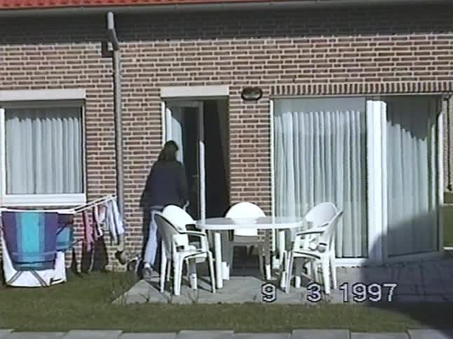 A woman walks inside her apartment from the backyard patio in a vintage home video from 1997