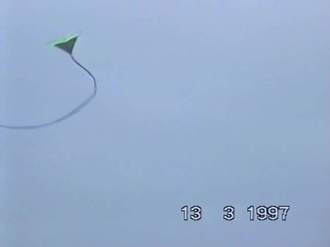 A vintage home video from 1997 shows a colorful kite soaring in the grey sky before it comes crashing down to the ground