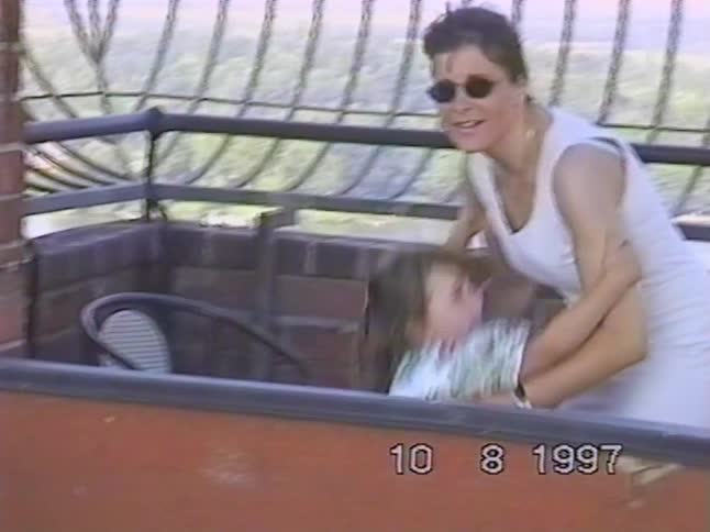 A vintage 1997 clip shows a mother and daughter smiling and posing for the camera on a windy observation tower overlooking a scenic landscape