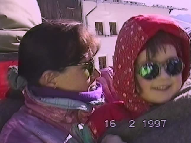 Vintage 1997 footage of a loving mother and daughter cuddling for warmth during a sleigh ride through a snowy mountain village