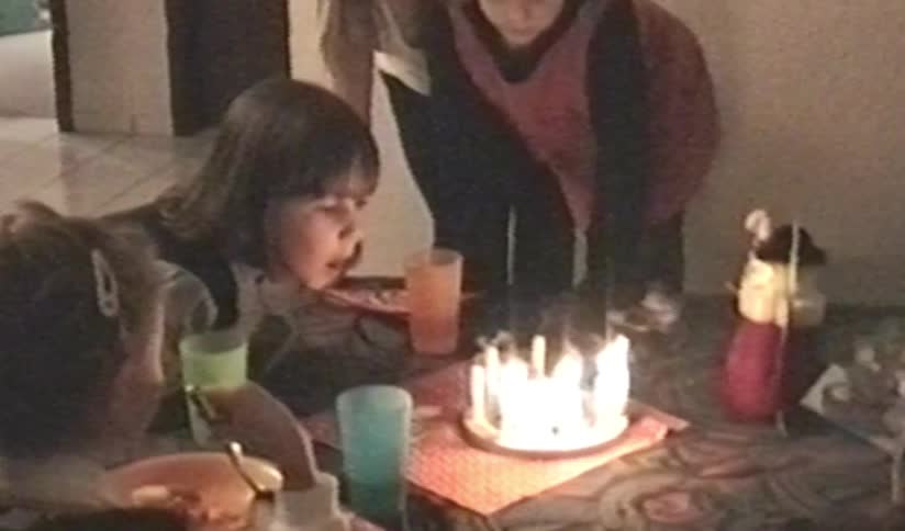 Vintage VHS footage from the 1990s shows a young girl blowing out the candles on her birthday cake