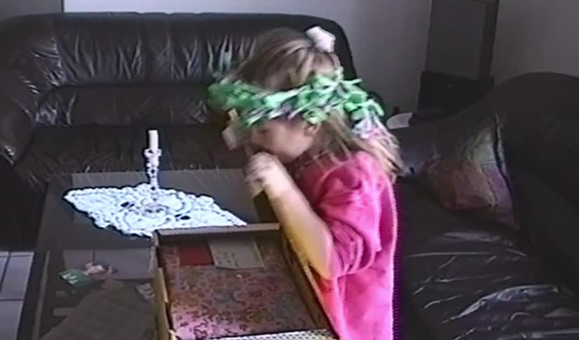 An excited young girl wearing a party crown opens a large gift box in this authentic vintage home video